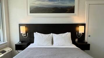 Een hotelkamer met een groot bed, twee nachtkastjes met lampen, een lijst met een landschap boven het bed en een deur aan de rechterkant.