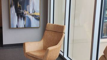 A modern interior with a large abstract painting, two brown armchairs, and a large window providing a view.