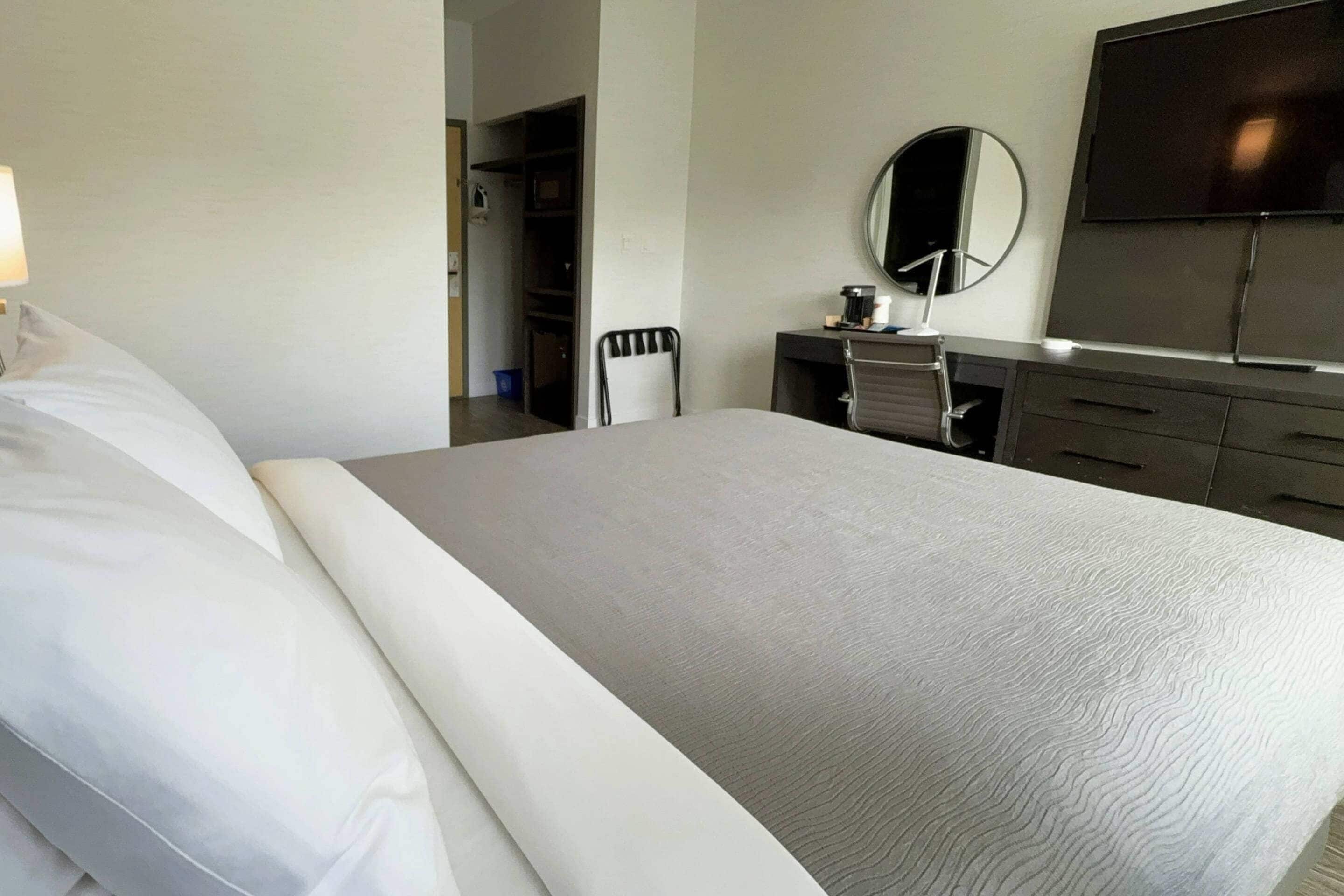 A hotel room with a bed, a desk with a chair, a TV, and a mirror.