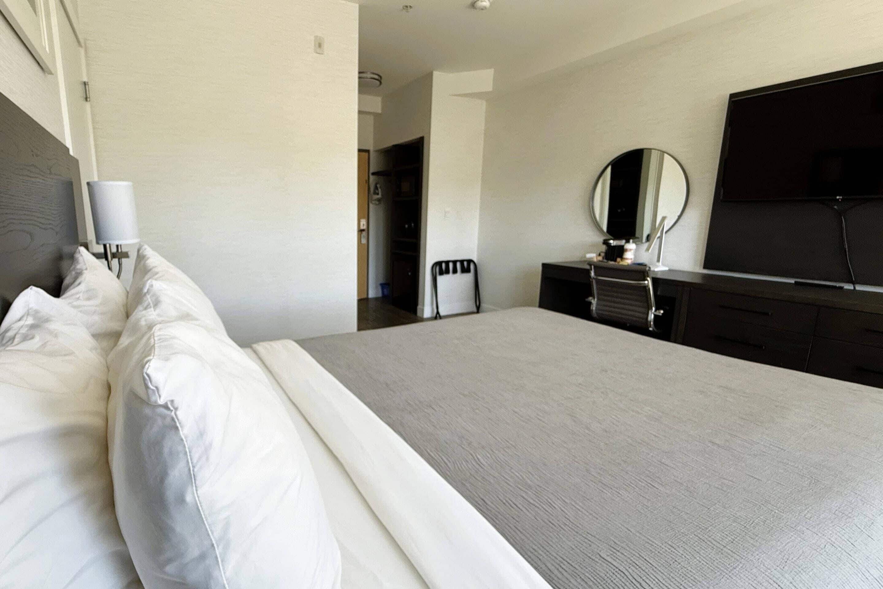 A modern hotel room with a large bed, a flat-screen TV, a dresser, and a mirror.
