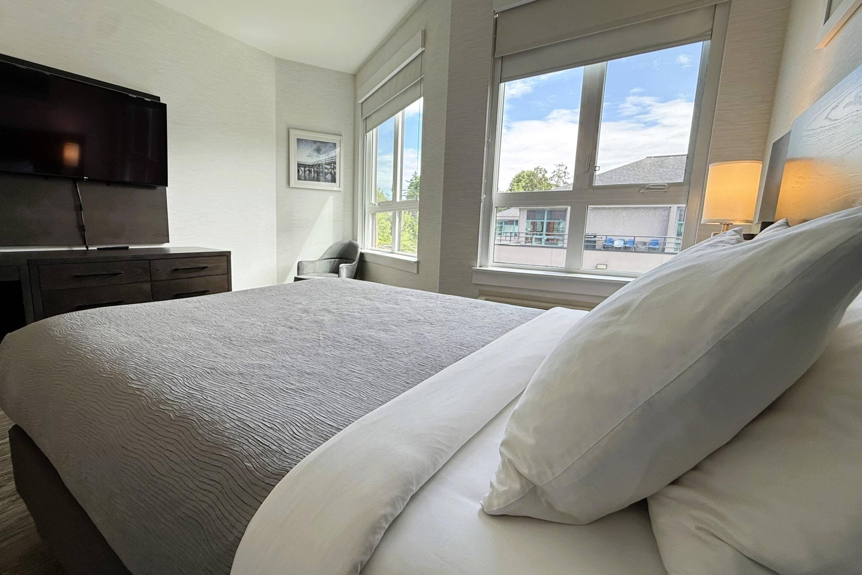 A hotel room with a bed, a flat-screen TV, a desk, a chair, and a window with a view of buildings.