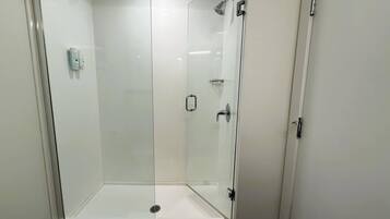 A glass-enclosed shower with a white door, a visible light switch, and a drain at the bottom.