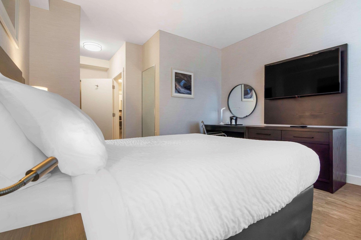 A hotel room with a large bed, a flat-screen TV, a desk with a chair, and a mirror.