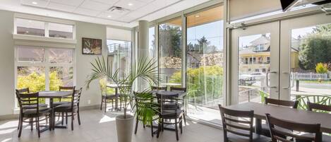 A spacious indoor area with multiple tables and chairs, large windows, and potted plants.
