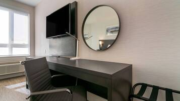 Een moderne hotelkamer met een bureau, stoel, televisie en een ronde spiegel.