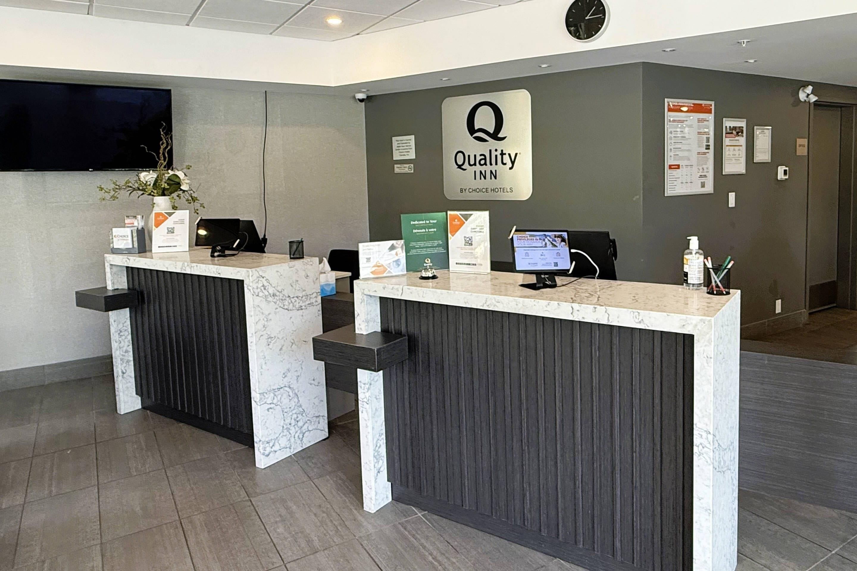 Mostrador de recepción de hotel con encimera de mármol, un reloj y un letrero de Quality Inn by Choice Hotels.