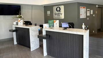 Mostrador de recepción de hotel con encimera de mármol, un reloj y un letrero de Quality Inn by Choice Hotels.