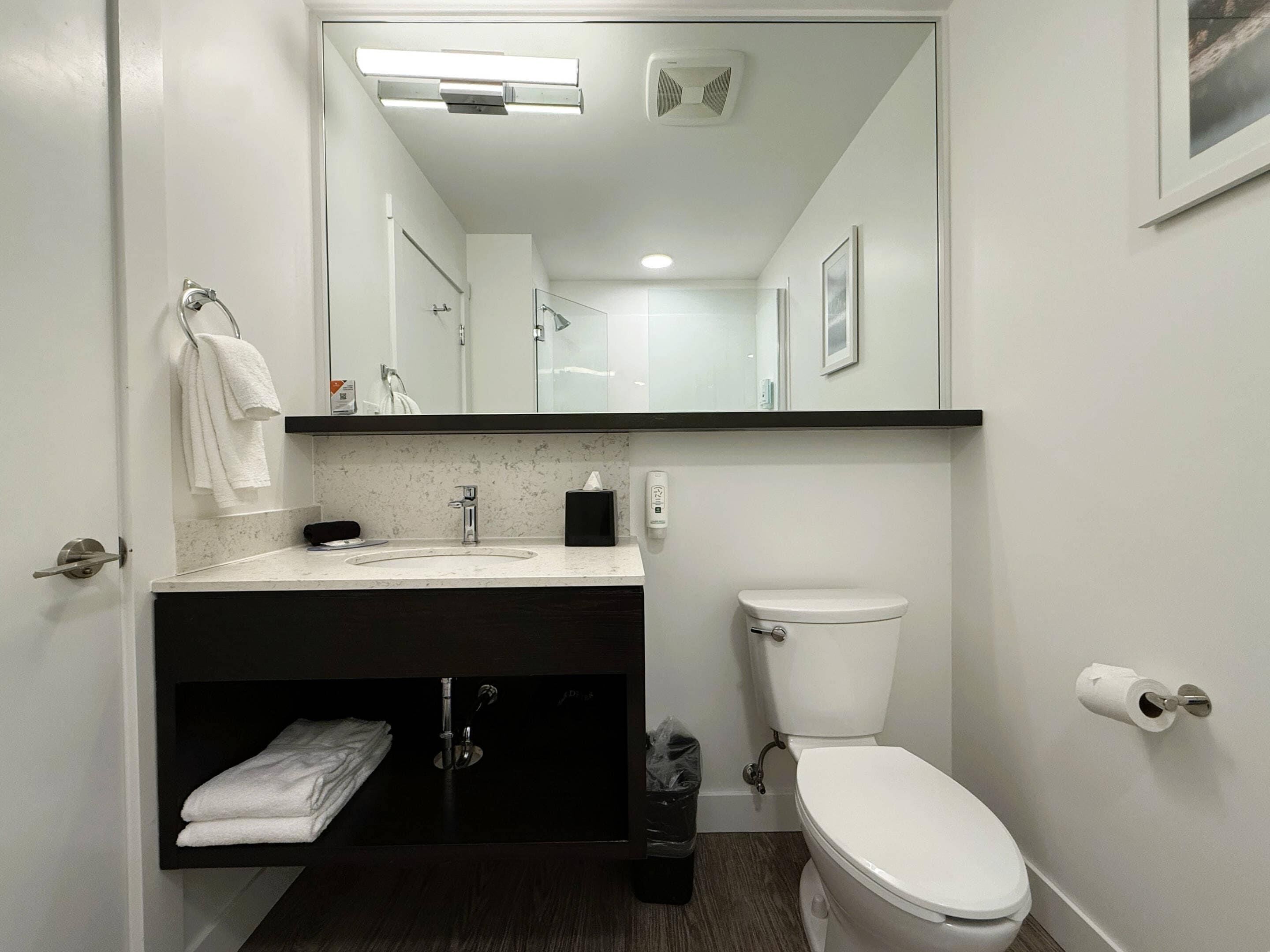 A bathroom with a white sink, mirror, toilet, and a trash bin.