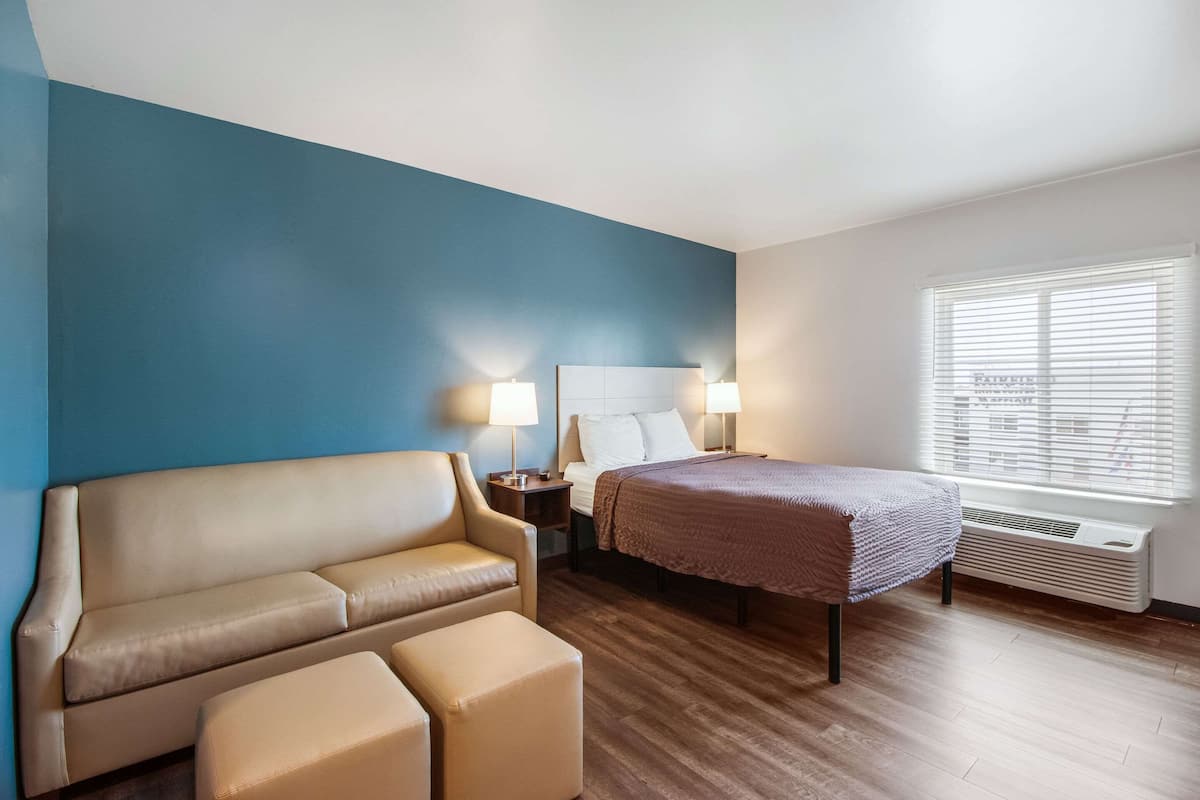 Une chambre d’hôtel avec un mur d’accent bleu, un lit recouvert d’une couverture marron, un canapé beige et une petite table avec des lampes.