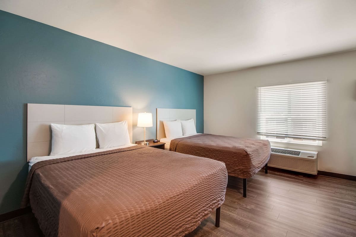 Une chambre d’hôtel avec deux lits, une fenêtre avec des stores, un radiateur et une table de chevet avec une lampe.