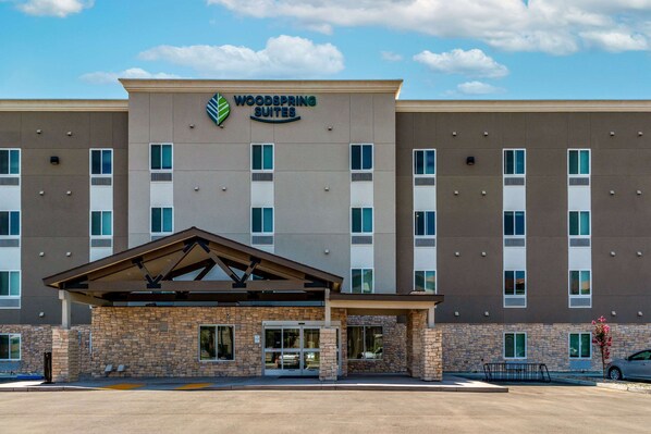 A hotel with a stone facade, a flat roof, and a sign reading "Woodspring Suites".