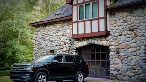 A black SUV parked in front of a stone building with a Tudor-style window and a stone facade. - 'The Castle Gatehouse' of Highlands Castle (Bolton)