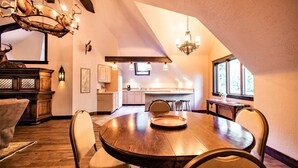 A dining area with a round wooden table, chairs, and a chandelier. There is a kitchen in the background with a window. - 'The Castle Gatehouse' of Highlands Castle (Bolton)