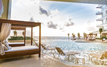A poolside area with a wooden canopy bed, lounge chairs, and a view of the ocean.