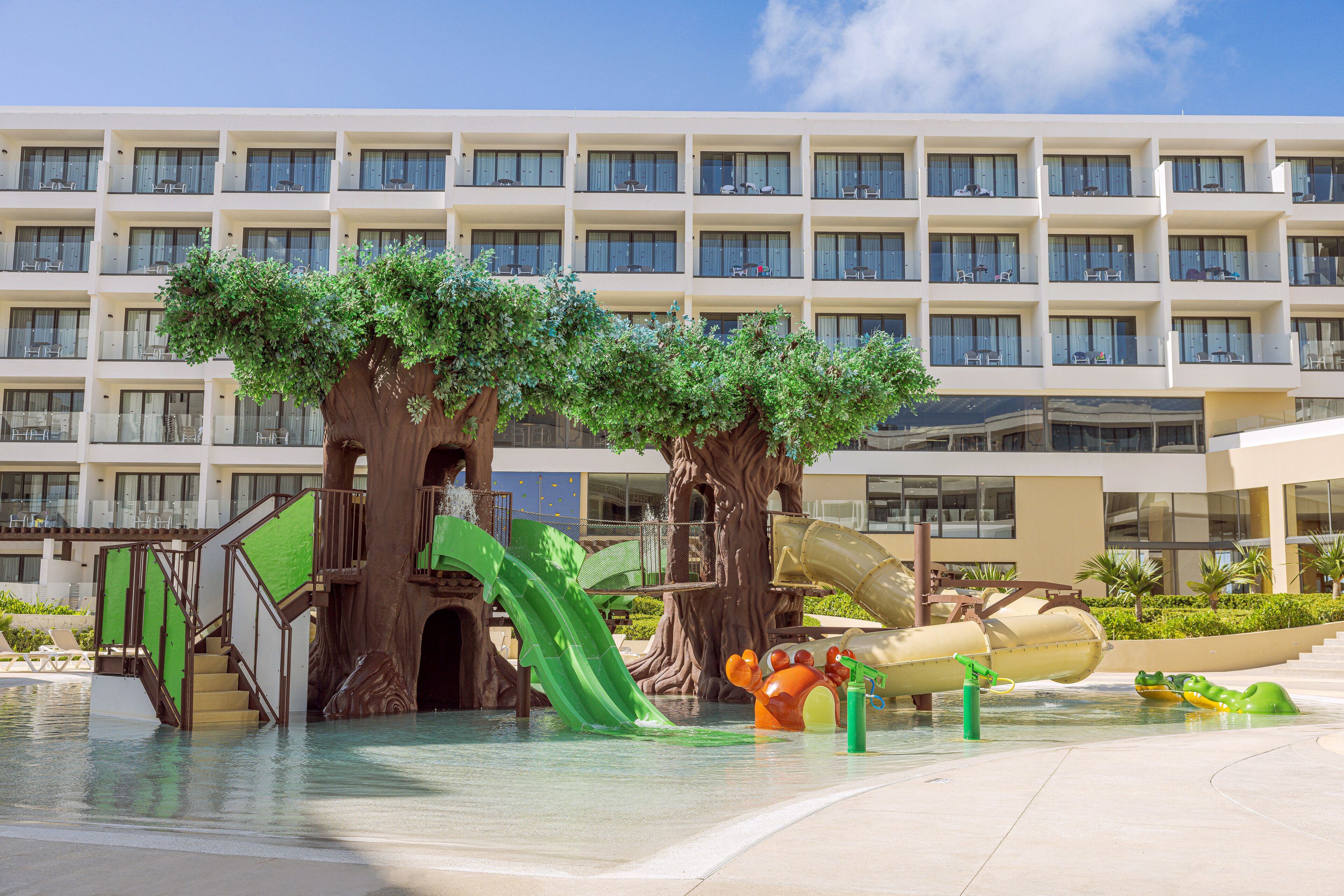 Een hotel met een waterpark met glijbanen en kunstbomen.
