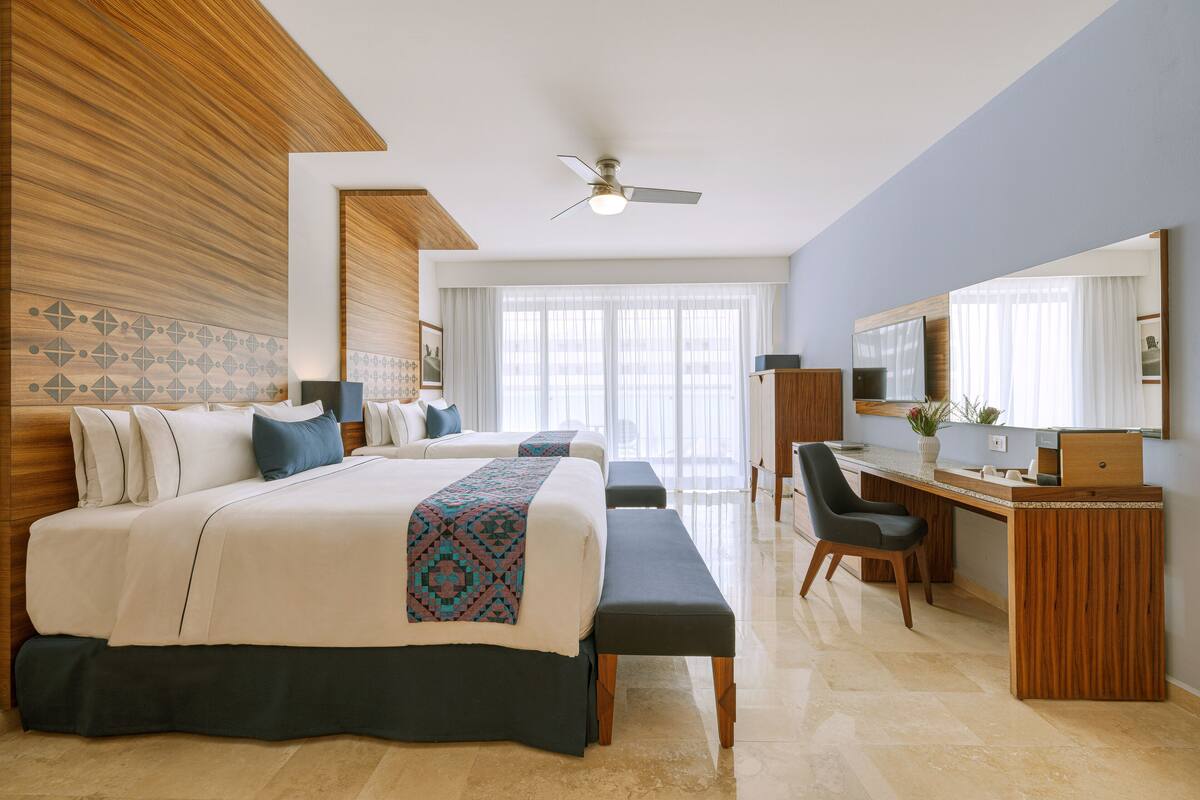 A modern hotel room with a large bed, a desk, and a ceiling fan.