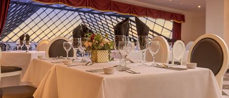 A dining area with tables set for a meal, featuring white tablecloths, neatly arranged cutlery, and a vase with flowers.