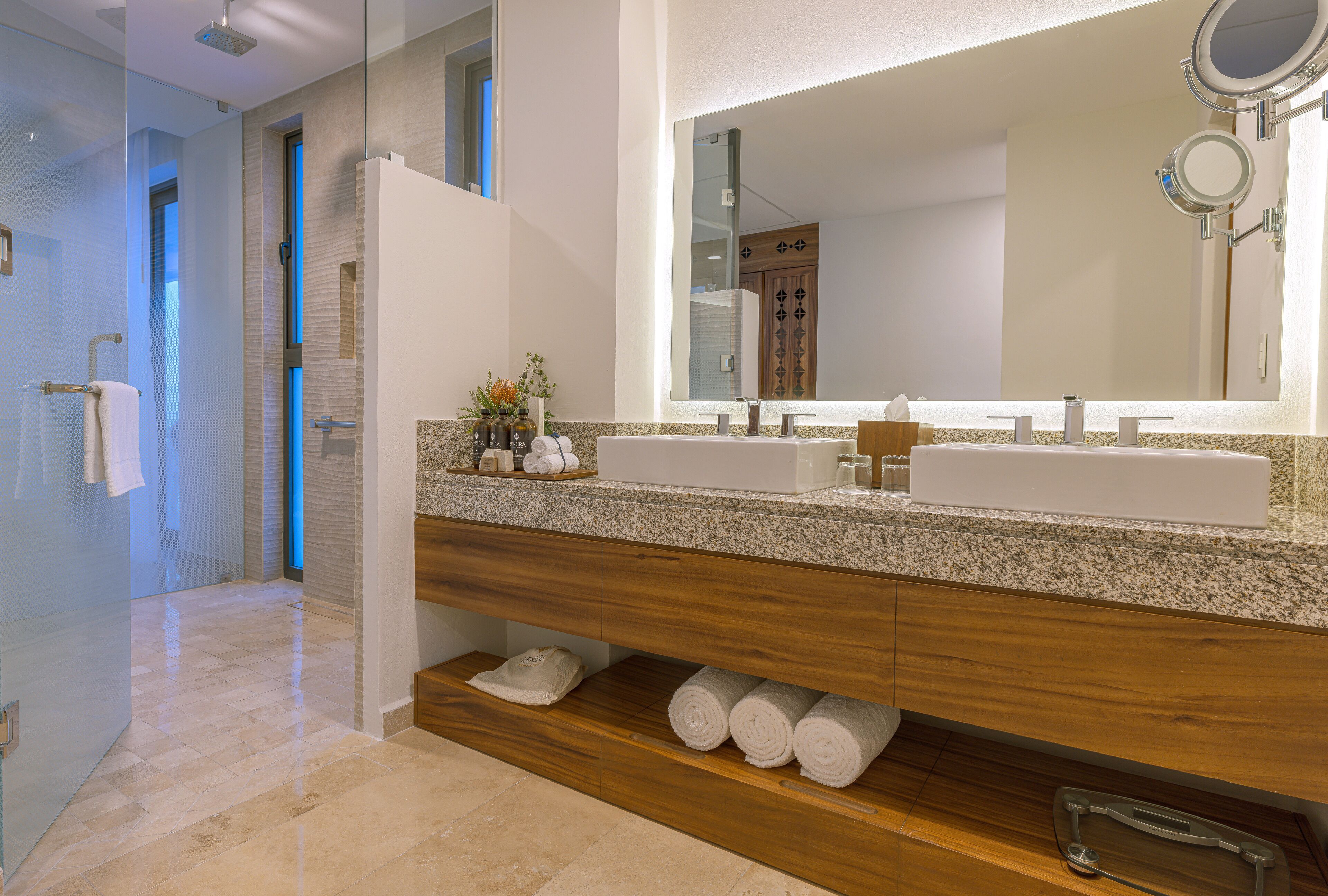 A modern bathroom with a large mirror, two sinks, and a wooden vanity.