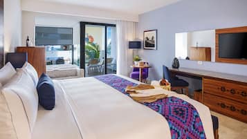 A hotel room with a large bed, a desk, a chair, a TV, and a balcony with a view.