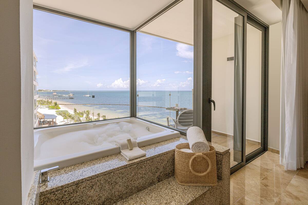 A balcony with a large bathtub, a wicker basket, and a view of the beach and ocean.