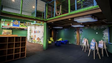 A children's play area with a netted ceiling, bean bags, and easels with drawings.