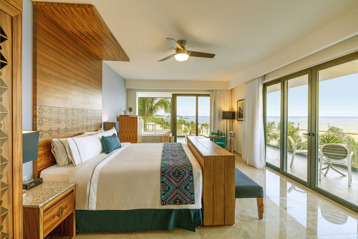A hotel room with a large bed, a desk, and a balcony with a view of the ocean.