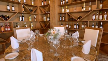 A dining table set with wine glasses, plates, and cutlery, surrounded by wooden shelves stocked with wine bottles.