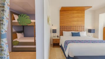 A hotel room with a bunk bed, a single bed, a wooden headboard, a nightstand with a lamp, and a patterned throw blanket.