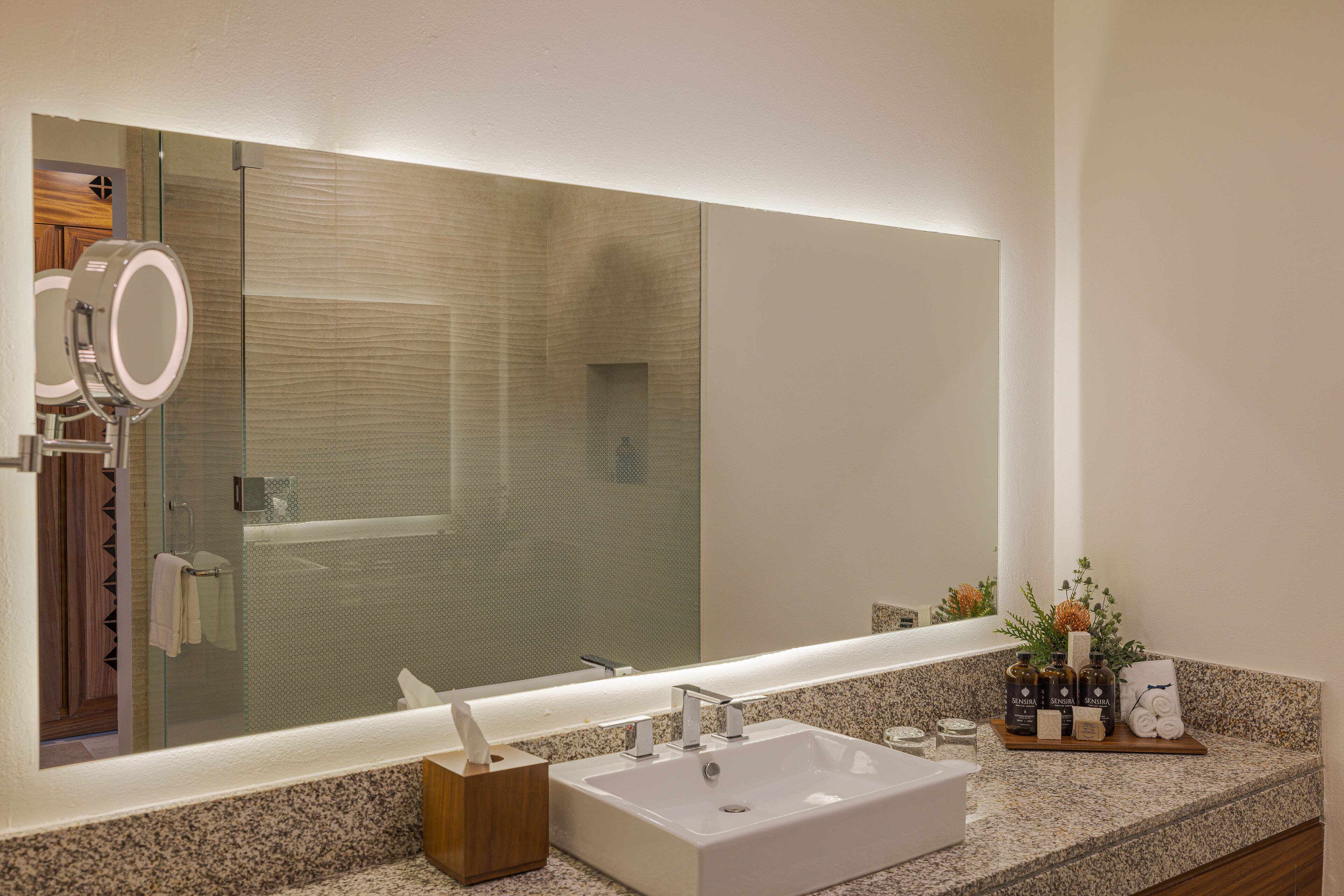 A modern bathroom with a large mirror, a rectangular sink, and a wooden tray holding toiletries.