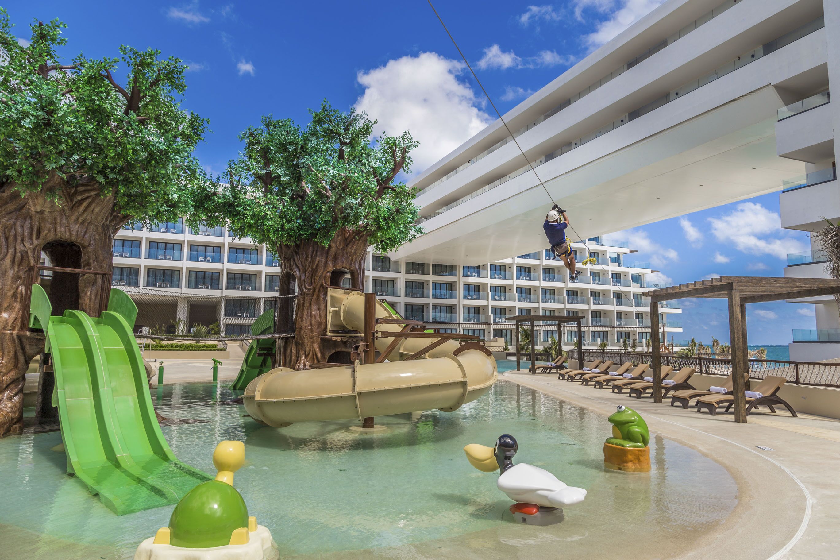 A water park area with slides, a lazy river, and a lifeguard on a suspended bridge.