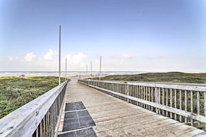 A wooden boardwalk leading to a beach with grassy dunes and a clear sky.