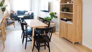 Una sala de estar moderna con comedor, que incluye una mesa y sillas de madera, un sofá y un televisor montado en la pared.