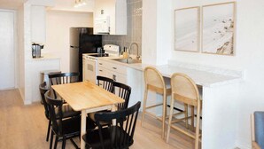 Una cocina moderna con gabinetes blancos, un refrigerador negro y una mesa de comedor de madera con sillas negras.