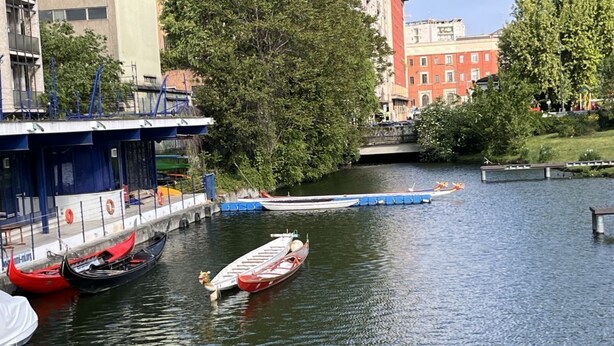 Un río con góndolas amarradas a un muelle, un puente al fondo y edificios a lo largo de la orilla.