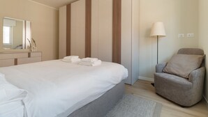 Un dormitorio con cama, una silla, una lámpara y un espejo.