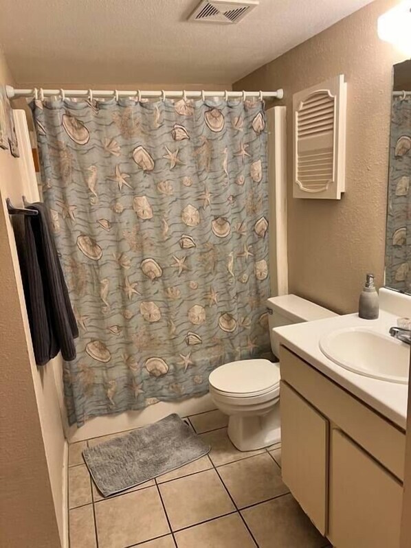 A bathroom with a shower curtain featuring a sea shell pattern, a toilet, a sink, and a mirror.