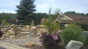 A stone wall with plants and an American flag, a large tree, and a building with a brown roof and a sign. - Dells Resort - Free Mini Golf + Kayaks + NO daily fee D (Dellona)
