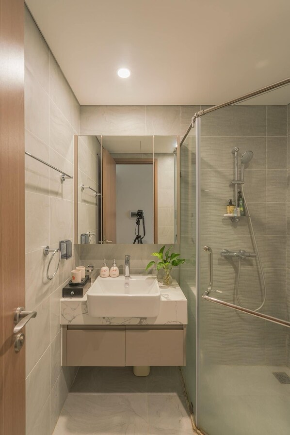 Un baño moderno con ducha de vidrio, lavabo de mármol y un espejo sobre él.