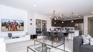 Een moderne woonkamer met een glazen salontafel, een grijze bank en een flatscreen televisie waarop geanimeerde figuren te zien zijn.