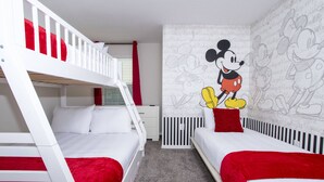 Een kinderkamer met stapelbedden, een muurschildering van Mickey Mouse en een ledikant.