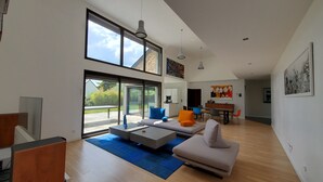 A spacious living area with a large window, a dining table, and a sofa. - Luxueuse villa, piscine intérieure, plage à 700m (Saint Coulomb)