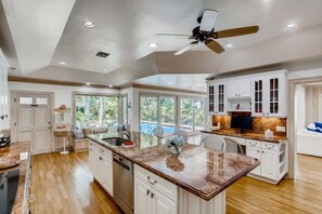 Una cocina amplia con una isla central, armarios blancos y un ventilador de techo.