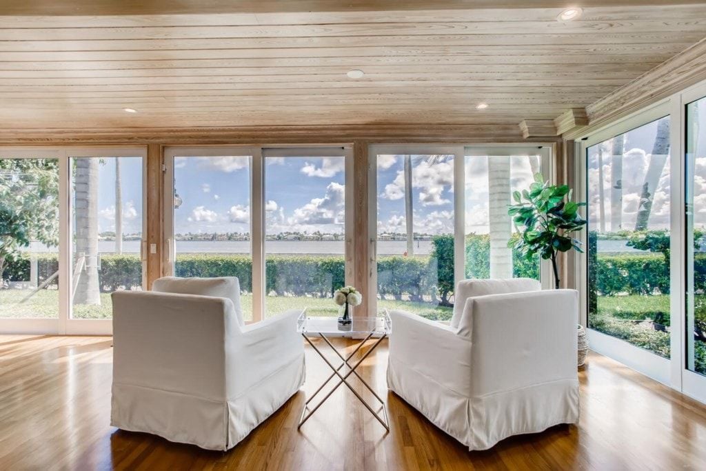 Ein Zimmer mit zwei weißen Stühlen, einem Glastisch und Blick auf eine Landschaft durch große Fenster.