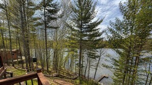 A wooden deck overlooking a lake with trees and a cabin. - Iggy & Al's Treehouse: Northwoods Getaway (Hazelhurst)