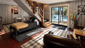 A bedroom with a bed, a wooden staircase, a dining table, and a view of the outdoors. - Iggy & Al's Treehouse: Northwoods Getaway (Hazelhurst)