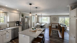 A spacious kitchen with a central island, wooden bar stools, pendant lighting, and a view to a balcony. - Iggy & Al's Treehouse: Northwoods Getaway (Hazelhurst)