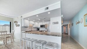 Una cocina moderna con armarios blancos, una isla central con taburetes y vistas al exterior.