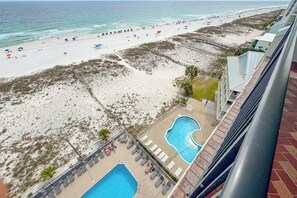A beach view from a hotel balcony, a swimming pool, and a sandy beach with umbrellas.
