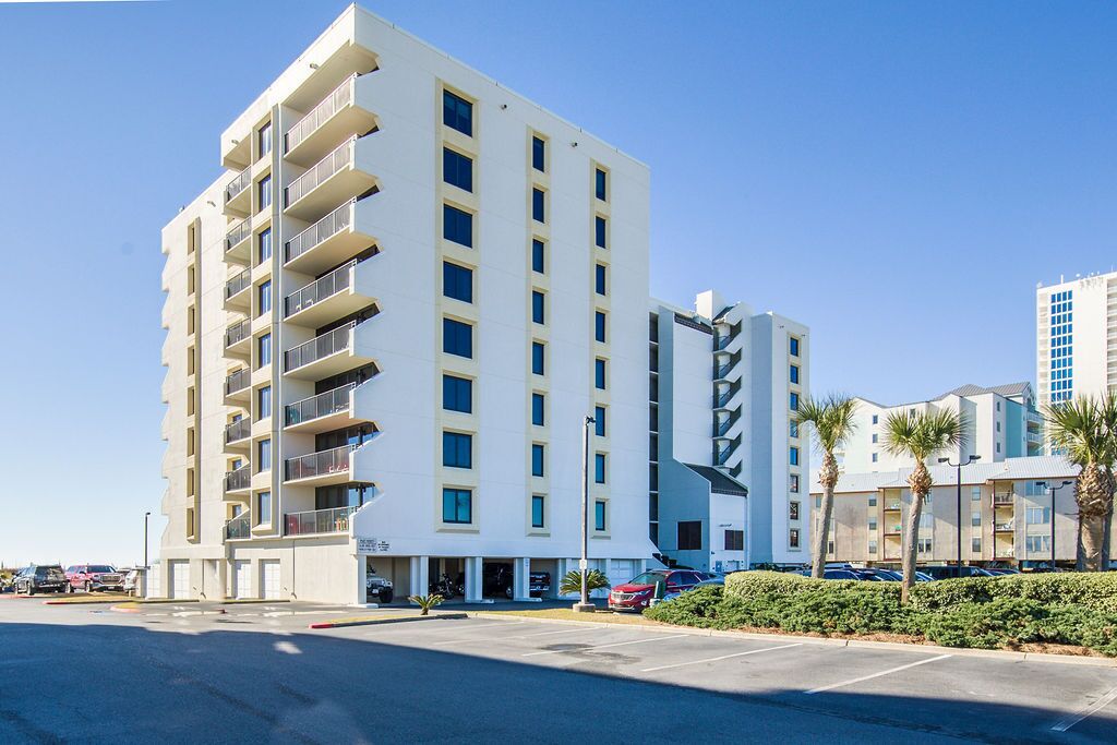 Ein mehrstöckiges Hotel mit Balkonen, einem Parkplatz und Palmen.