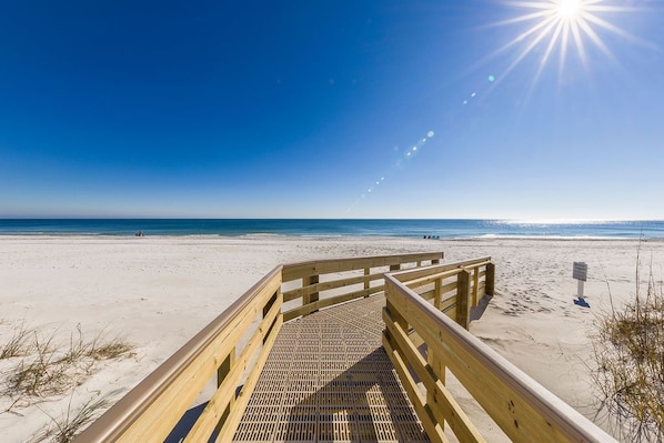 A wooden boardwalk leading to a beach with a clear sky and sun shining.